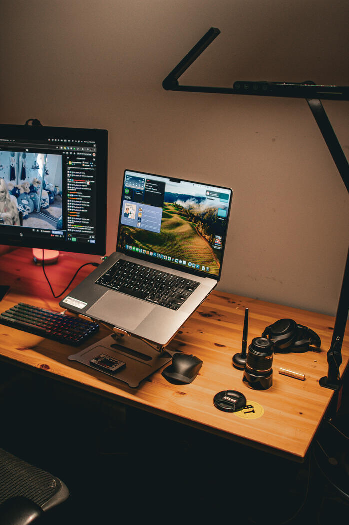 Photograph of a wooden desk with a MacBook Pro and drawing monitor in set in spot light.